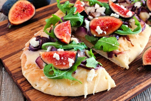 Autumn flat bread pizza with figs, caramelized onions, arugula and cheese, close up on serving board
