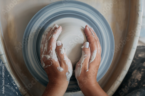 Top view of pottery wheel with woman hands, dirty hands of potter