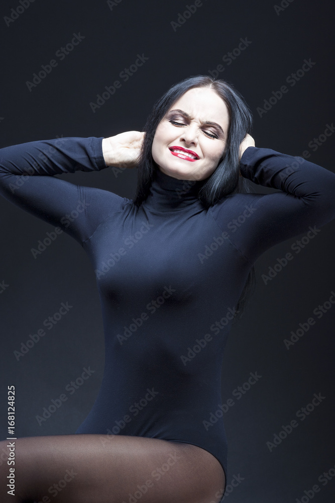 Portrait of Screaming Caucasian Mature Brunette. Posing in Black Body suit Against Black.
