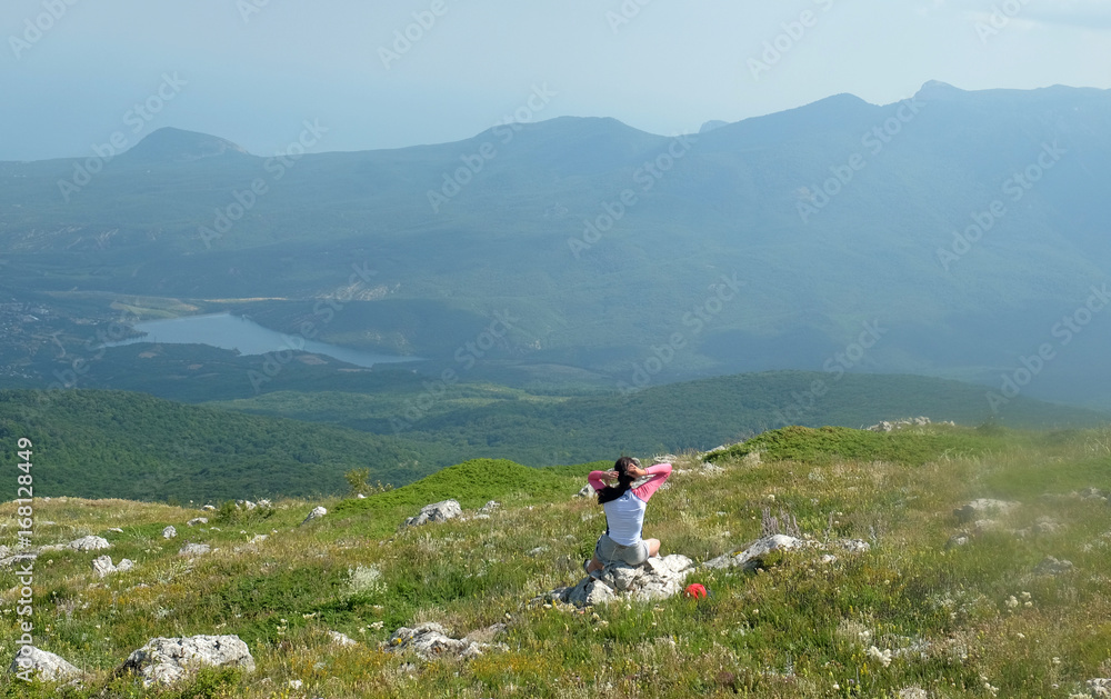 Naklejka premium A young girl sits on edge cliff and looking at mountain landscape