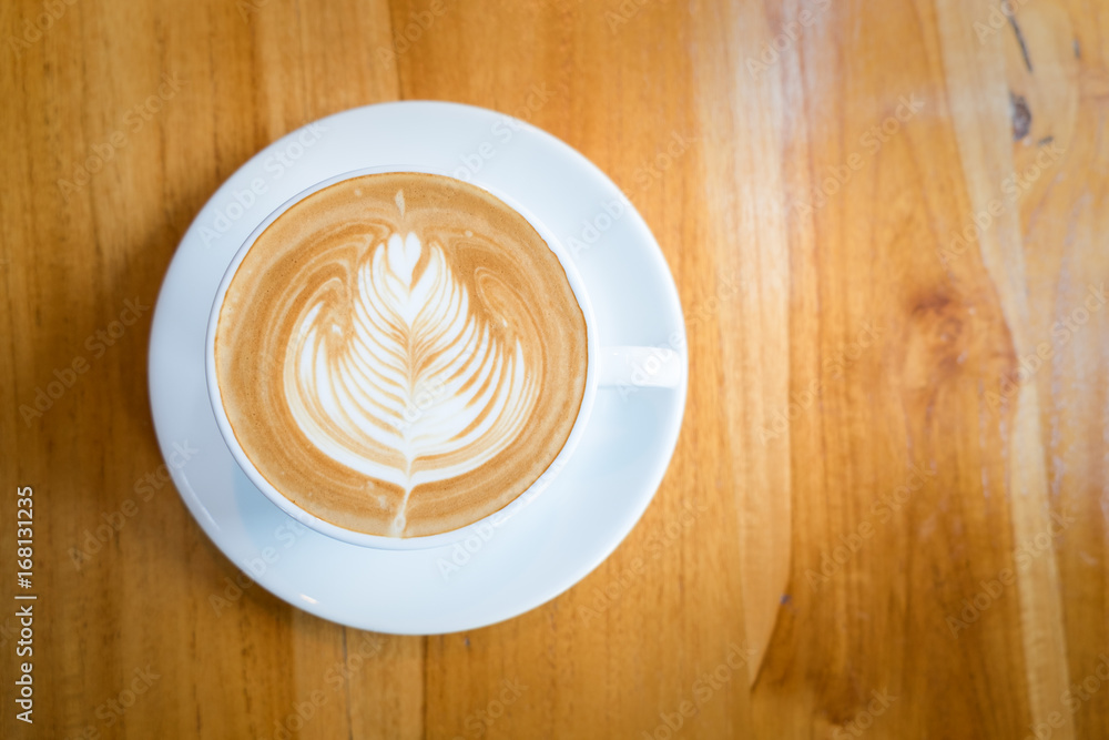 A white cup of hot latte art coffee on the wooden table in coffee cafe A white cup of hot latte art coffee on the wooden table in coffee cafe
