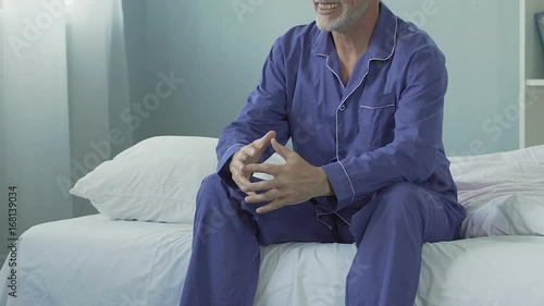 Energetic man sitting on bed in morning smiling and stretching, happy retirement photo