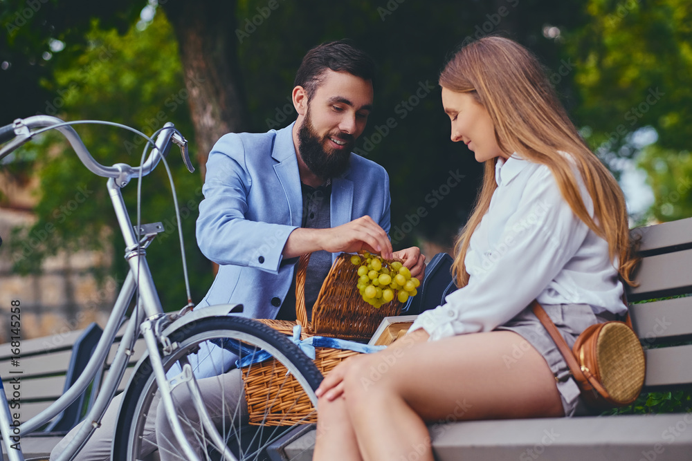 Obraz premium A couple eats grape on a bench in a park.