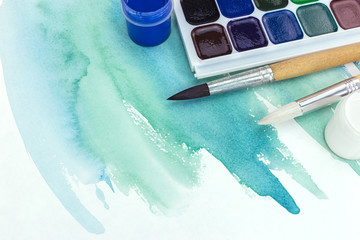 green watercolor painting on paper with paint palette and paintbrushes 