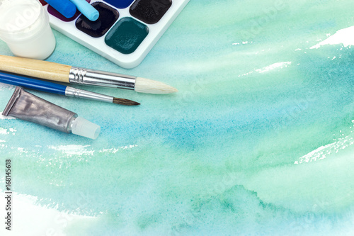 artistic paintbrushes and paints on abstract green watercolor background