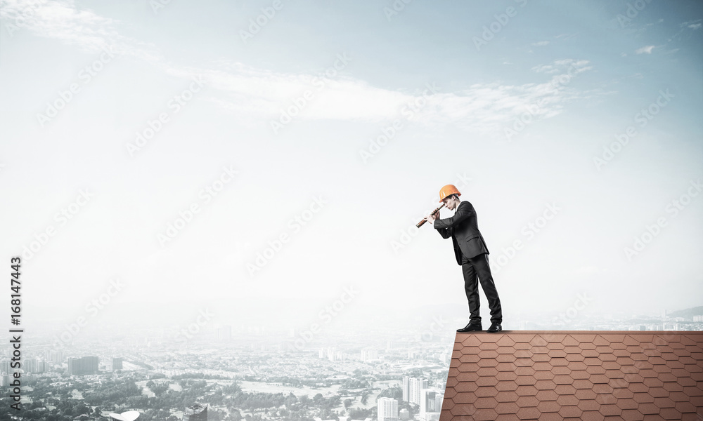 Engineer man standing on roof and looking in spyglass. Mixed med