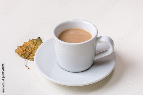 Isolated cup of coffee on saucer with autumn fallen yellow leaf on white background.