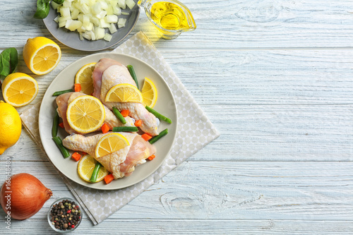 Raw chicken drumsticks with lemon and ingredients on light wooden table