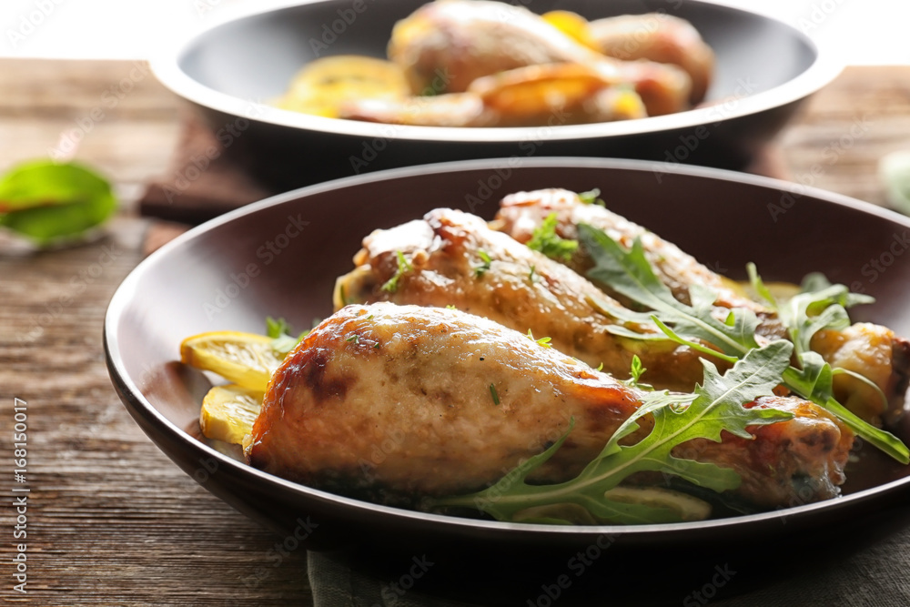 Plate with delicious roasted chicken drumsticks and sliced lemon on wooden table Plate with delicious roasted chicken drumsticks and sliced lemon on wooden table