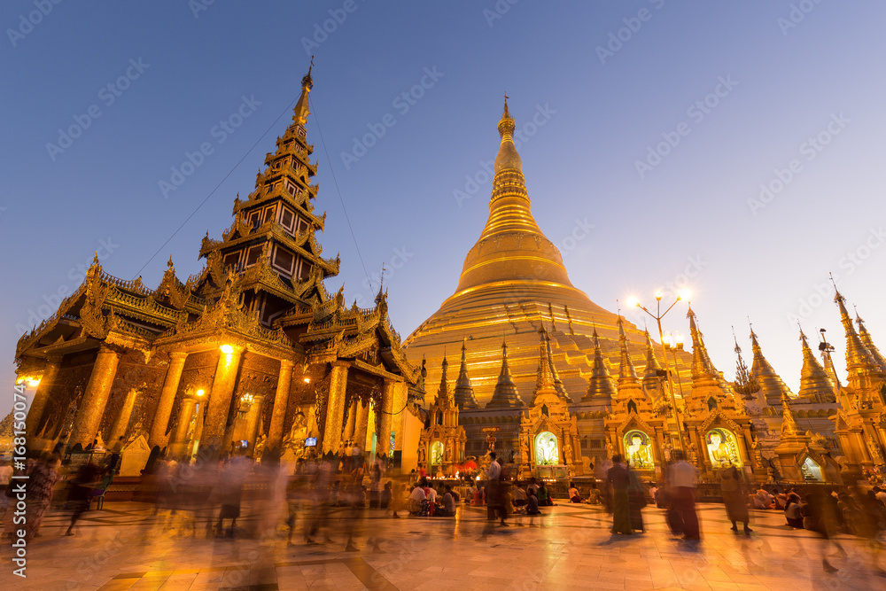 A lot of people in front of the gilded and lit Shwedagon Pagoda in Yangon, Myanmar, at dawn.