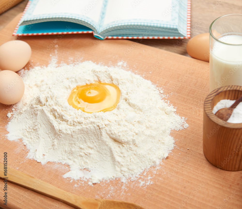 Flour heap and broken egg closeup for baking on a wooden background. Raw food and kitchen utensils. Flour heap and broken egg closeup for baking on a wooden background. Raw food and kitchen utensils.