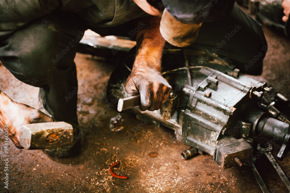 Mechaniker bearbeitet mit öligen Händen mit einem Hammer und einem