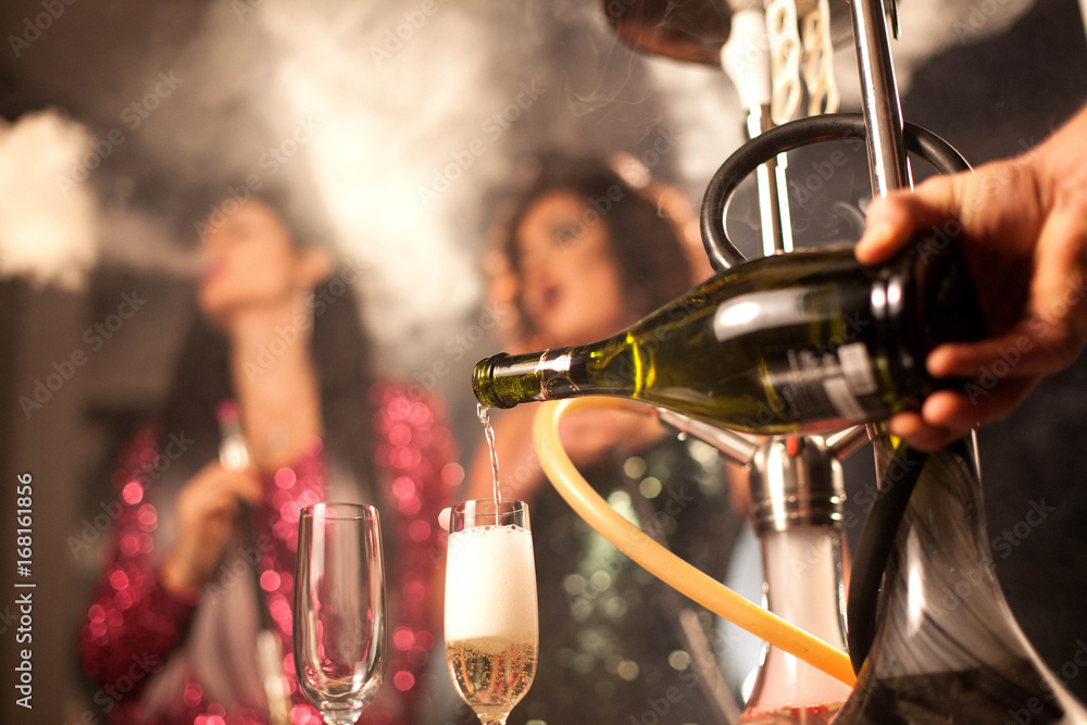 Wine or champagne pouring from bottle into a glaas. Two girls smoking