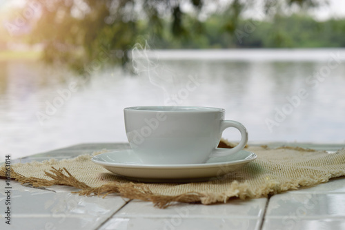 Wallpaper Mural hot coffee in white cup on table with lake and trees nature background. Torontodigital.ca