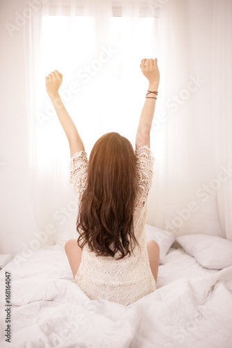 Woman stretching in bed after wake up, back view.