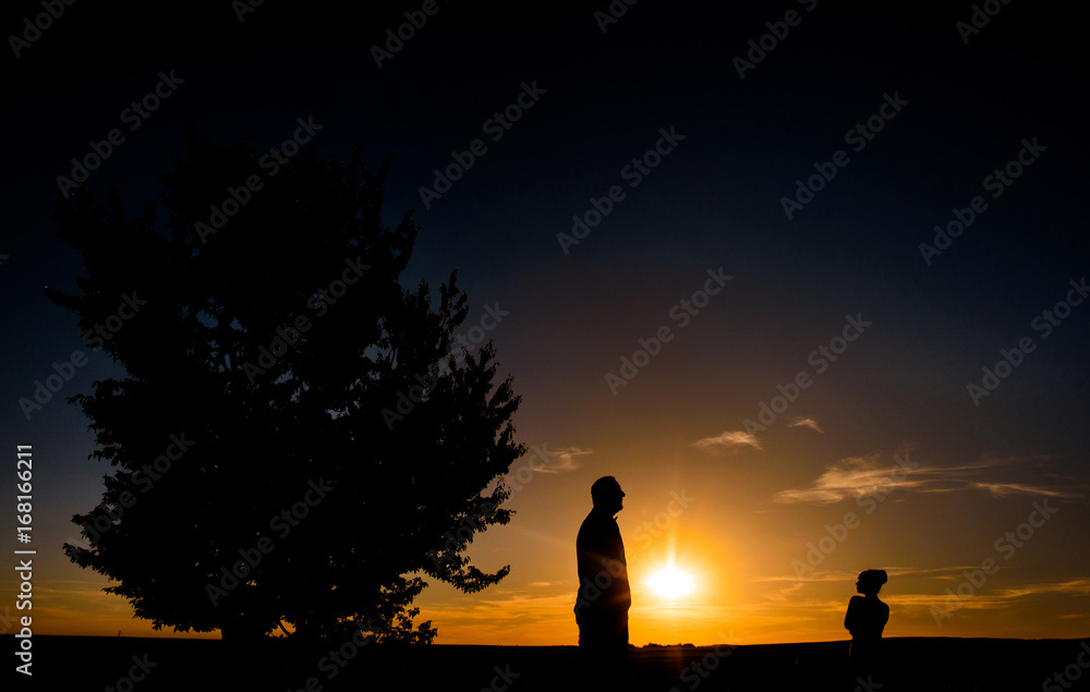 Silhouettes of man and girl standing on a field before a sunset