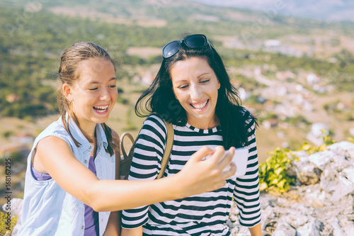 Mother and daughter photographing, taking a selfie on mountain peak, whilst resting
