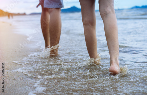 Close up lower body man and girl couple walking at beach in sunlight