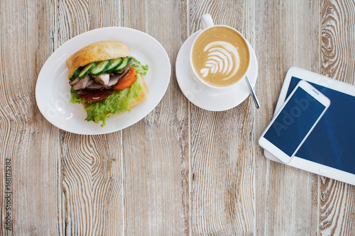 Delicious breakfast on the table. Chicken sandwich, Cup of coffee and smartphone on the table photo