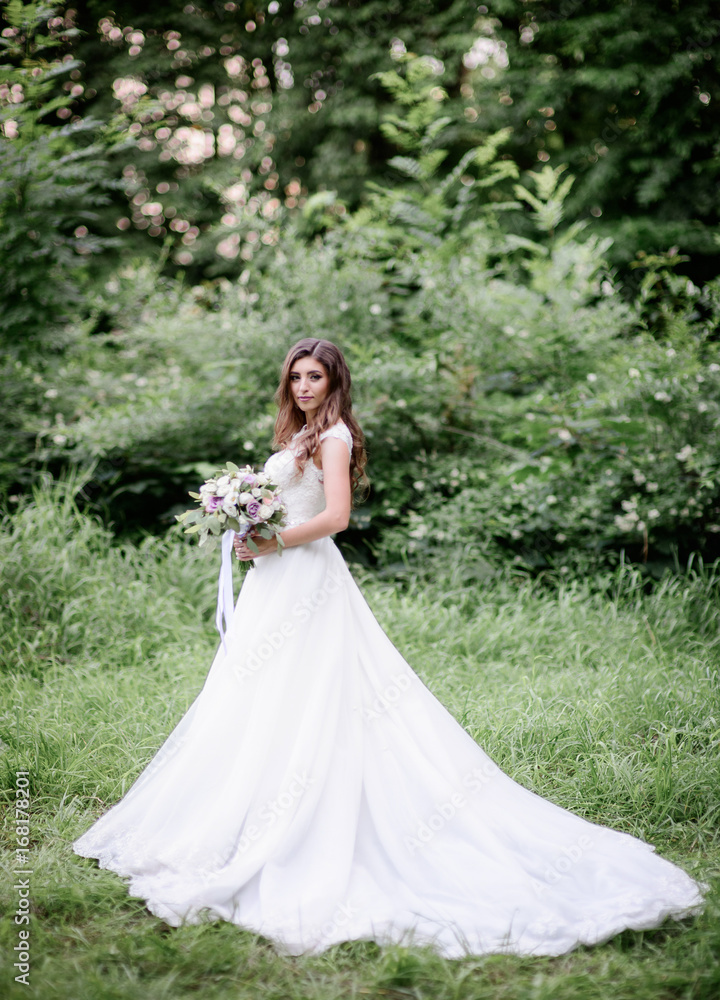 Tender bride in a long dress poses in a green garden