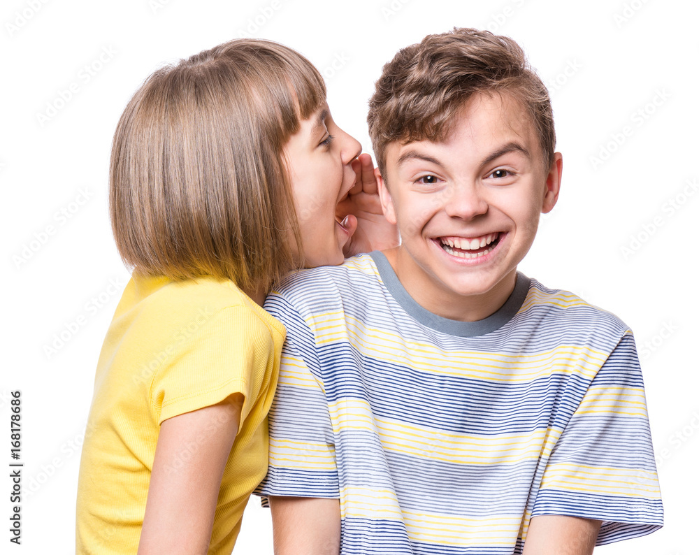 Friendship - beautiful girl whispering something to teen boy. Portrait of happy brother and sister, isolated on white background. Funny couple children - first love.