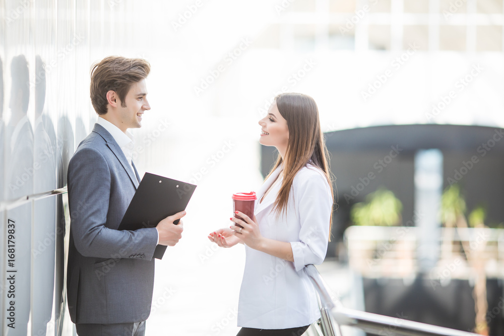 Two Business Colleagues standing in office hall having informal discussion with coffee Two Business Colleagues standing in office hall having informal discussion with coffee