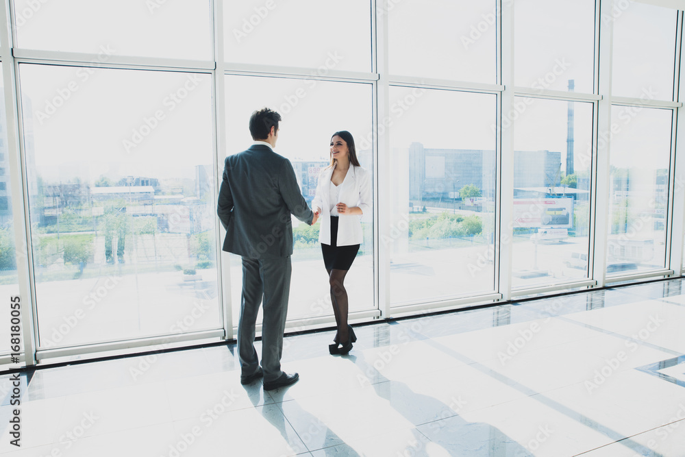 Two young businessman and business woman are standing in modern office with panoramic windows.