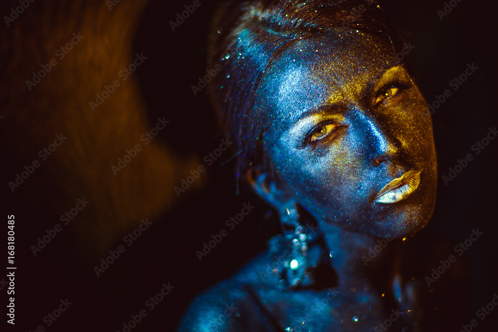 Woman covered with a bronze paint shines in the rays of a light