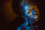 Woman covered with a bronze paint shines in the rays of a light