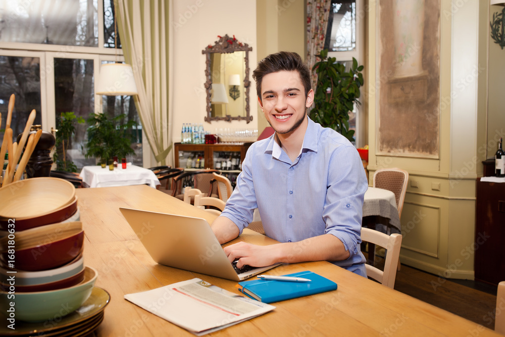 Young guy working on laptop in the Italian style kitchen Young guy working on laptop in the Italian style kitchen