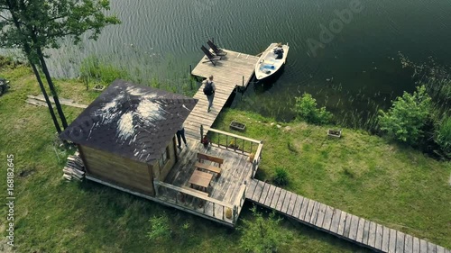Young just married couple in a boat near by small summer house on island. They are going back on the coast. Drone flying over.Upper view.