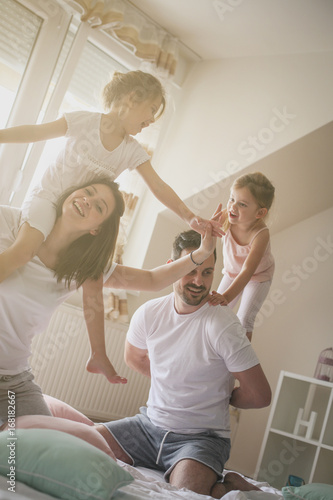 Family spending free time at home. Daughters sitting on the shoulders of their parents. Fun on bed. Girls sitting on parents shoulders.