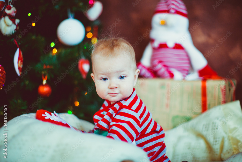 Little boy in stripped pyjamas sits before a Christmas tree Little boy in stripped pyjamas sits before a Christmas tree