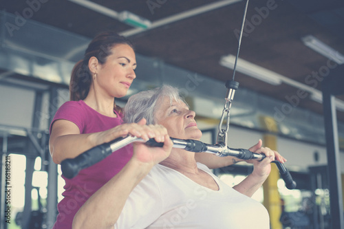 Active senior woman working exercise in the gym. Personal trainer helping senior woman. Workout in gym.