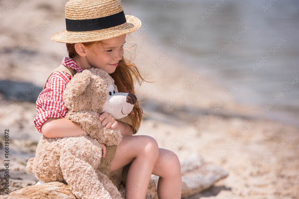 child with teddy bear at seashore