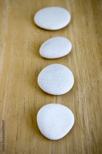 Row of white zen stones on wooden mat, five pebbles in a row, massage pebbles, low depth of field