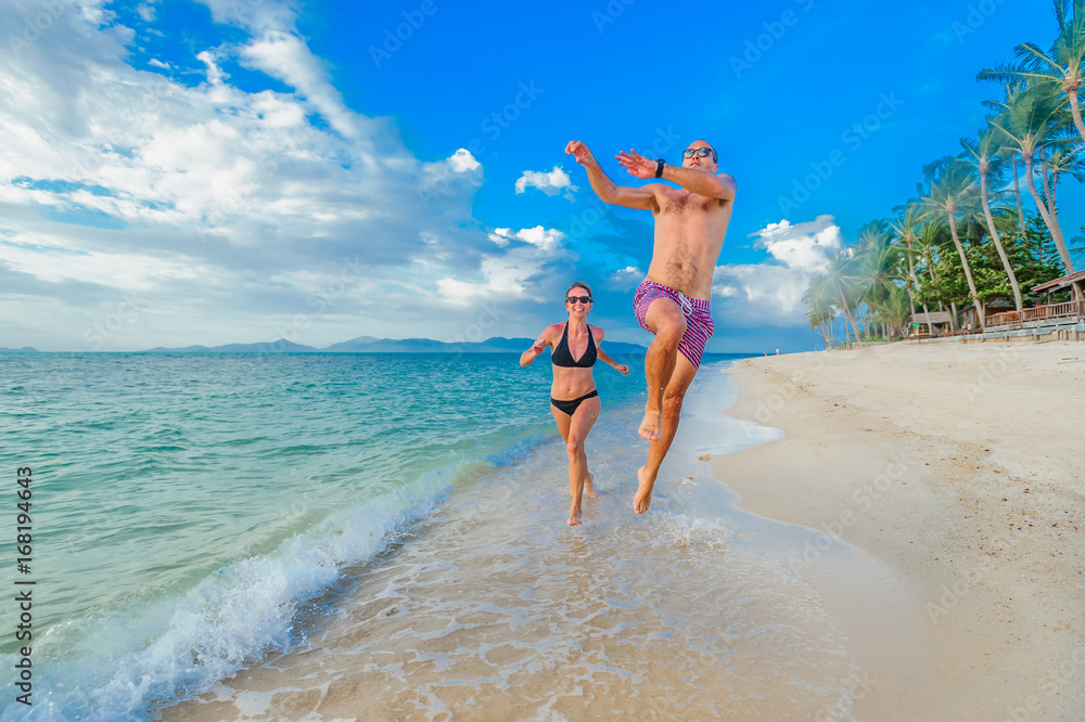 Childhood in the soul: a couple of thirty-year-olds jumping and running along the tropical beach, fighting and doing a handstands, laughing and having fun