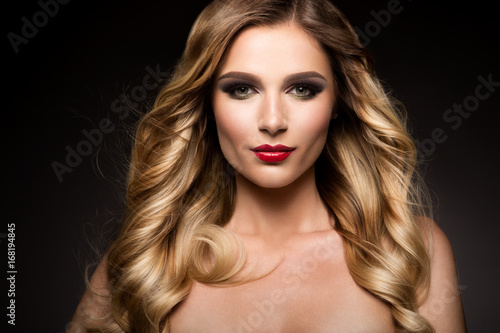 Beautiful blonde model girl with long curly hair . Hairstyle wavy curls . Red lips . Fashion , beauty and make up portrait