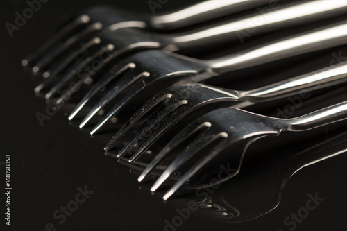 Metal shiny forks isolated over black reflective background with copy space