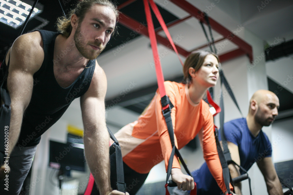 Friends doing exercises in a gym with straps. Three friends in the gym.