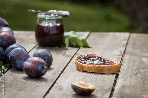 Sandwich with plum jam on old wooden table in garden.
