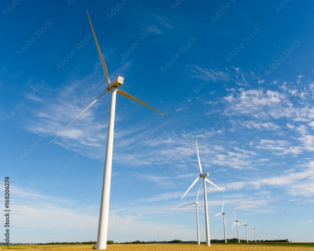 Alignment of wind turbines amid the fields generating renewable electricity from the wind. Alignment of wind turbines amid the fields generating renewable electricity from the wind.
