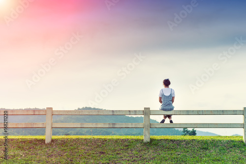 Young woman sitting on fence and sunlight