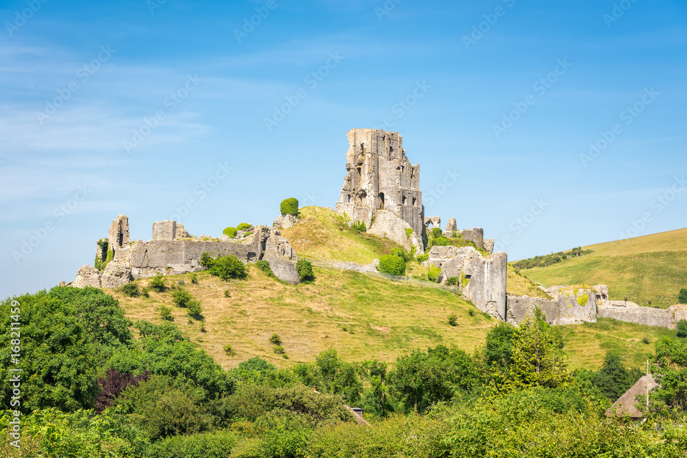 Wareham, United Kingdom - June 20, 2017: Ruins of Corfe Castle, built by William the  Conqueror in the Isle of Purbeck in Dorset, viewed from the village below. Copy space in blue sky.