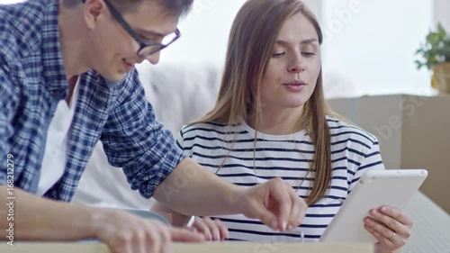 Medium shot of happy young woman with tablet giving instructions to cheerful boyfriend screwing bolts into wooden furniture