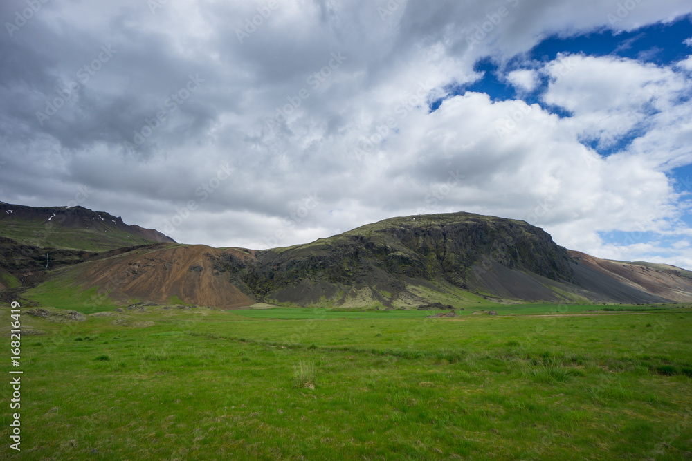 Iceland - Green volcanic mountains with meadow and cloudy sky