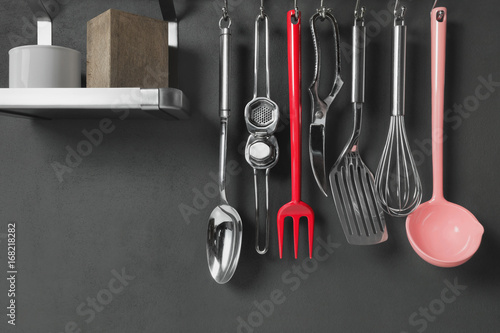 Kitchen utensils hanging with steel hooks, gray wall on background