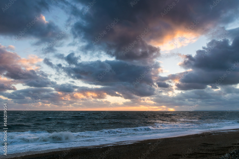 Storm clouds gather at sunset over rough sea from beach