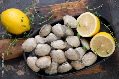 Above view of fresh unopened vongole shells with lemon and ice on a rustic wooden cutting board