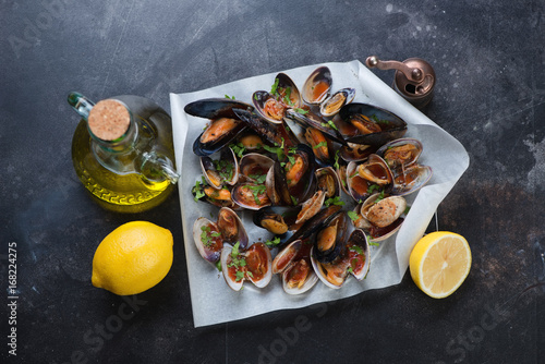 Baked vongole shells and mussels with olive oil and lemon, flat-lay over dark scratched metal background, horizontal shot